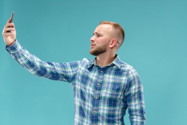 Free photo portrait of attractive young man taking a selfie with his smartphone. isolated on blue space.