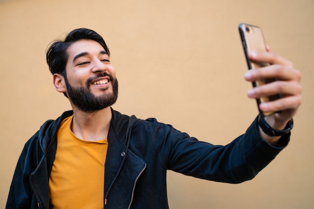 노란색 벽에 그의 mophile 전화 selfies를 복용하는 매력적인 젊은 남자의 초상화.