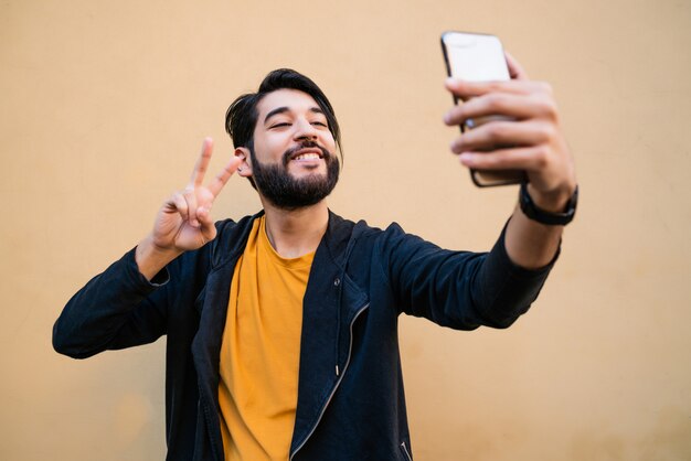 노란색 벽에 그의 mophile 전화 selfies를 복용하는 매력적인 젊은 남자의 초상화.