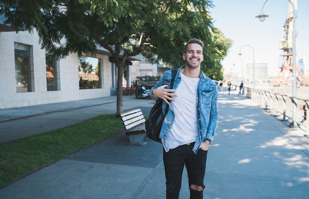 Portrait of attractive young man walking on the street with backpack on his shoulders. Urban concept.