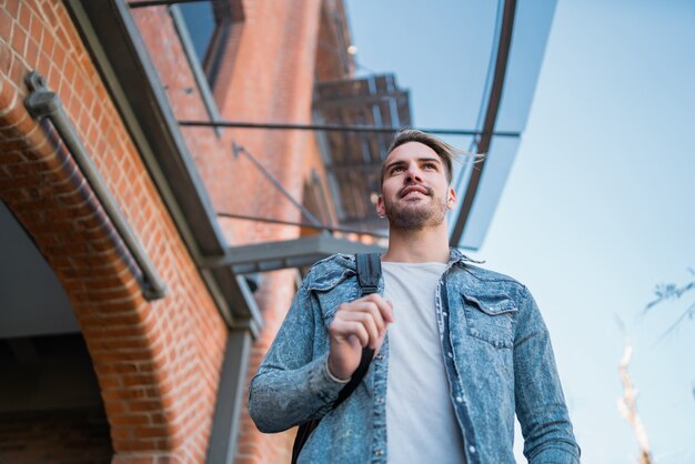 Portrait of attractive young man walking on the street with backpack on his shoulders. Urban concept.