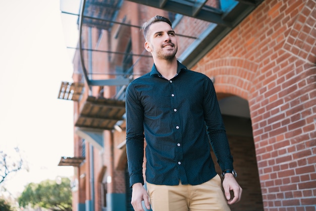 Portrait of attractive young man wearing casual clothes, standing outdoors with urban space.