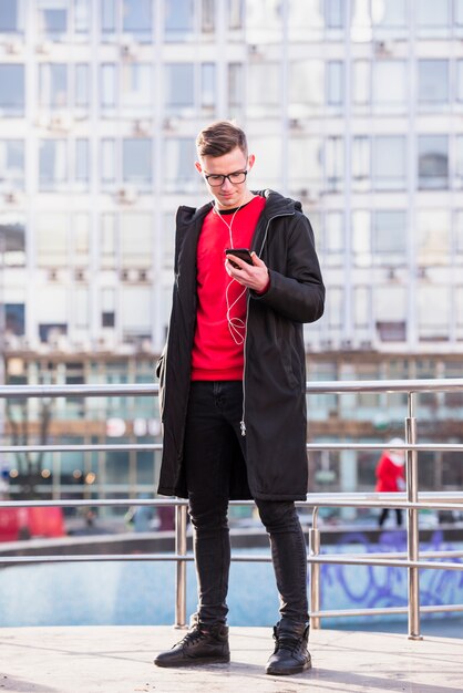 Portrait of an attractive young man wearing long jacket listening music on cellphone