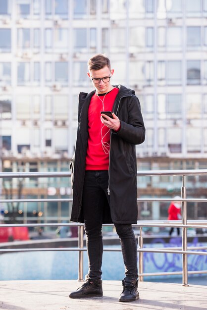 Портрет привлекательный молодой человек, одетый в длинную куртку прослушивания музыки на мобильном телефоне