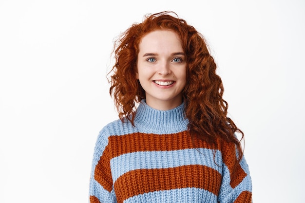 Ritratto di giovane donna attraente della testarossa con capelli sani ricci e occhi azzurri, denti bianchi sorridenti, guardando ottimista e gioioso su bianco