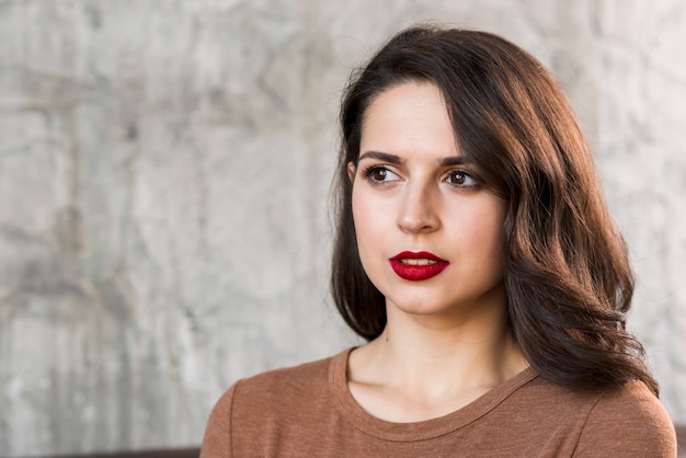 Foto gratuita ritratto di una giovane donna attraente che osserva via contro il muro di cemento