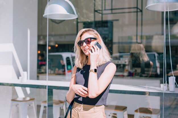 Free photo portrait of an attractive young woman standing in front of shop talking on mobile phone