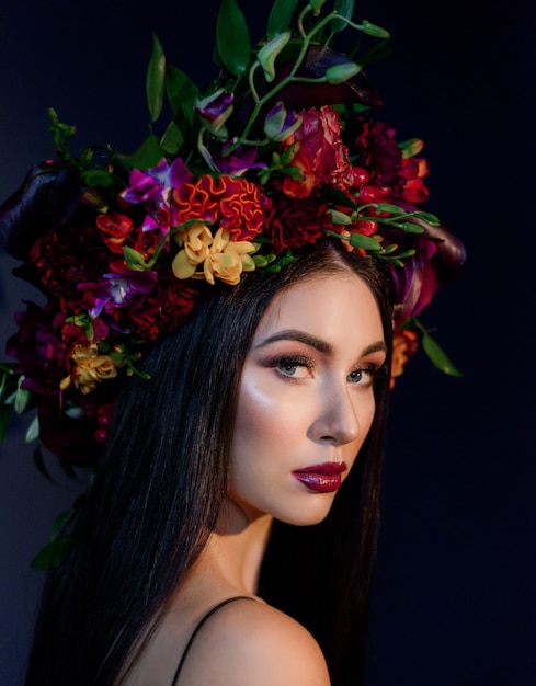 Portrait of attractive young woman with bright make-up dressed in big colorful floral wreath