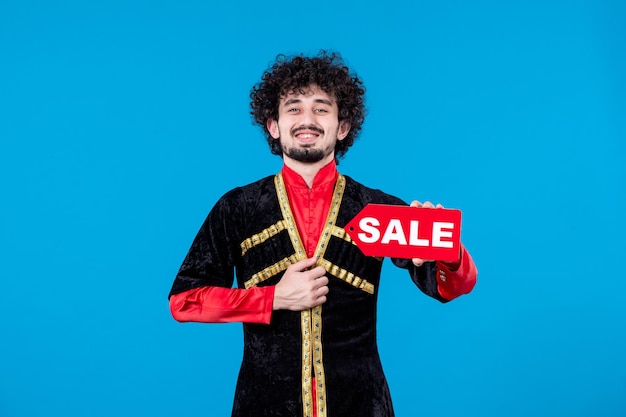 Portrait of azeri man in traditional costume holding sale nameplate on blue background ethnic spring shopping
