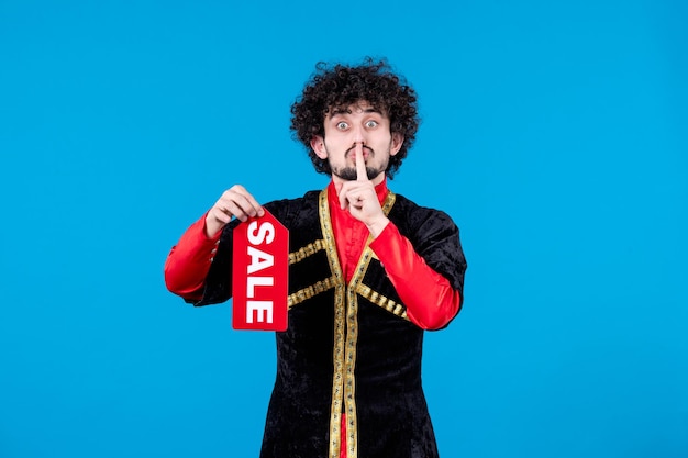 Portrait of azeri man in traditional costume holding sale nameplate on blue background novruz color ethnic spring shopping