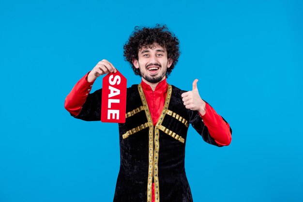 Portrait of azeri man in traditional costume holding sale nameplate on blue background novruz ethnic spring