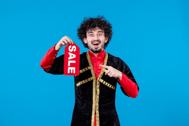 Portrait of azeri man in traditional costume holding sale nameplate on blue background novruz spring shopping