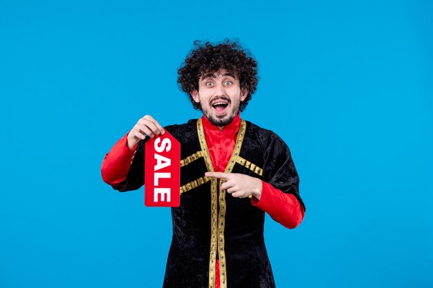 Portrait of azeri man in traditional costume holding sale nameplate on blue background spring novruz ethnic concept