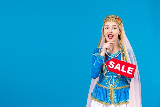 Portrait of azeri woman in traditional dress holding red sale nameplate on blue background ethnic novruz shopping spring color