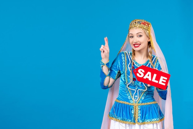 Portrait of azeri woman in traditional dress holding red sale nameplate on blue background ethnic shopping novruz