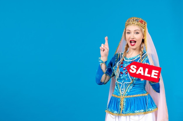 Free photo portrait of azeri woman in traditional dress holding red sale nameplate on blue background spring shopping novruz