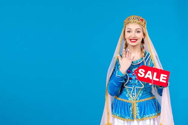 Free photo portrait of azeri woman in traditional dress holding sale nameplate blue background ethnic spring shopping dancer