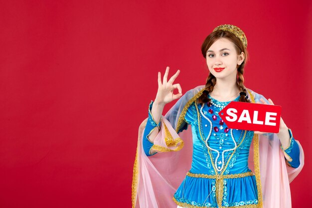 Portrait of azeri woman in traditional dress holding sale nameplate on red