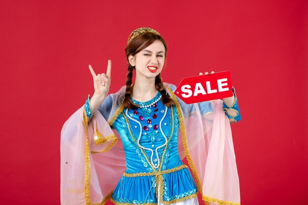 Portrait of azeri woman in traditional dress holding sale nameplate on red