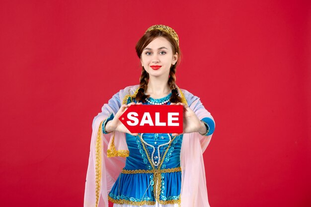 Portrait of azeri woman in traditional dress holding sale nameplate on red