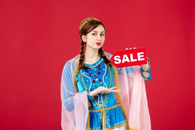 Portrait of azeri woman in traditional dress holding sale nameplate on red