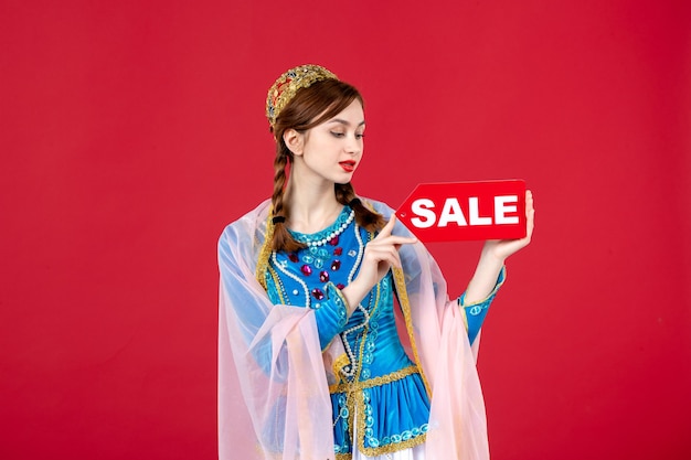 Portrait of azeri woman in traditional dress holding sale nameplate on red