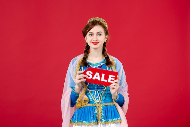 Portrait of azeri woman in traditional dress holding sale nameplate on red