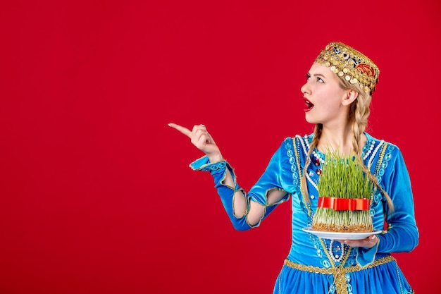 Free photo portrait of azeri woman in traditional dress holding semeni studio shot on red background concept novruz spring