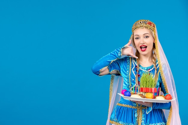 Free photo portrait of azeri woman in traditional dress with novruz xonca posing on blue background spring ethnic money