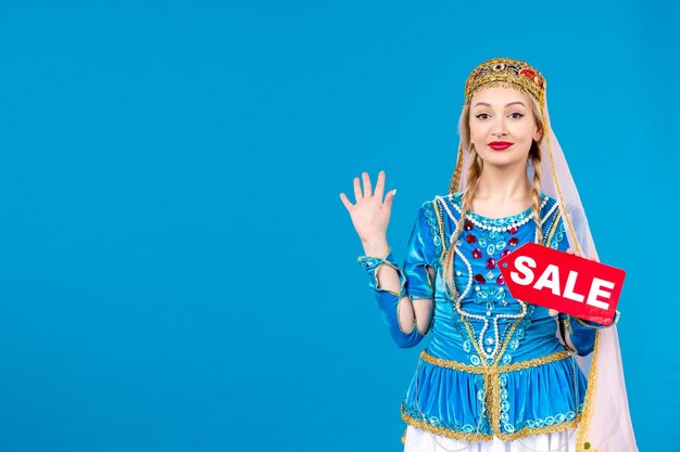 Portrait of azeri woman in traditional dress with sale nameplate blue background spring shopping dancer