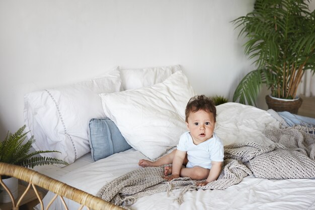 A portrait baby boy sitting upright on the bed