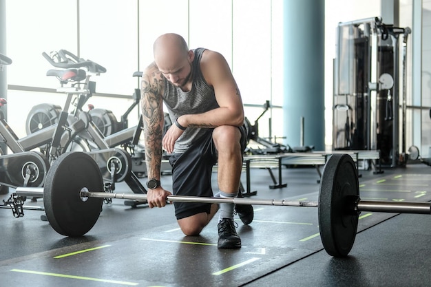 Portrait of a bald athletic man with a tattoo on his hand is preparing for the exercises with a barbell.