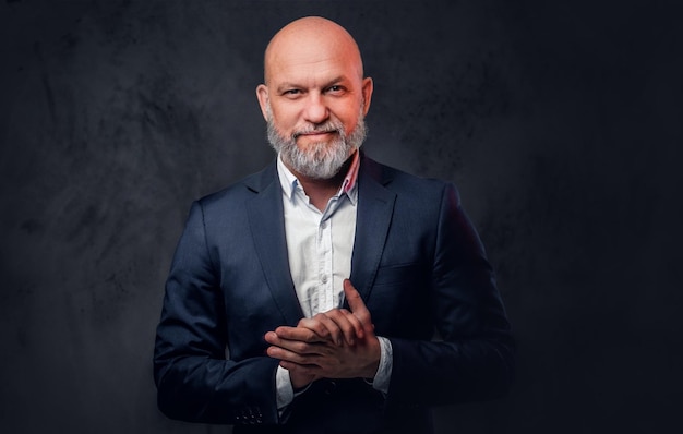 Portrait of bald senior dressed in stylish suit posing against dark background.