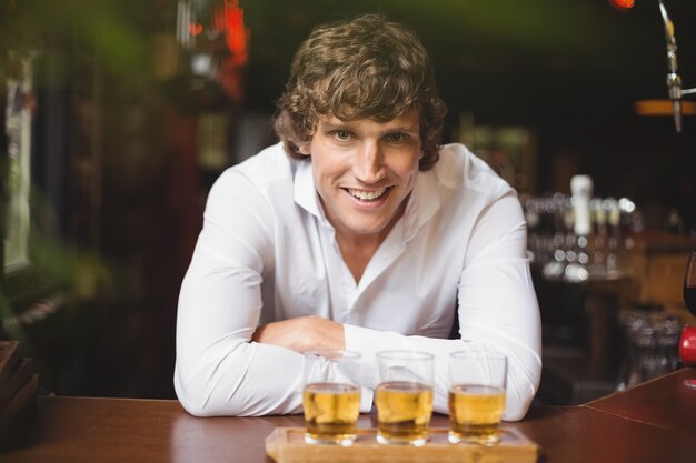 Portrait of bartender with tray of whisky shot glasses at bar counter