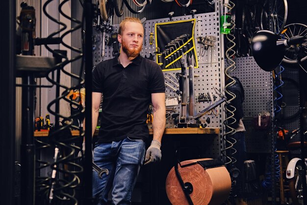 Portrait of bearded bicycle mechanic over tool stand background in a workshop.