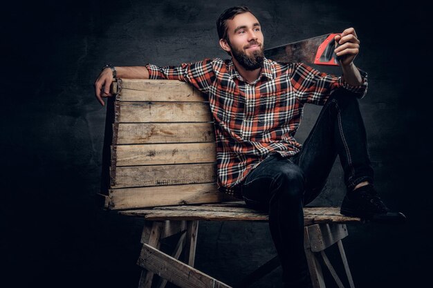 Портрет бородатого плотника в клетчатой рубашке и джинсах с ручной пилой на плече.