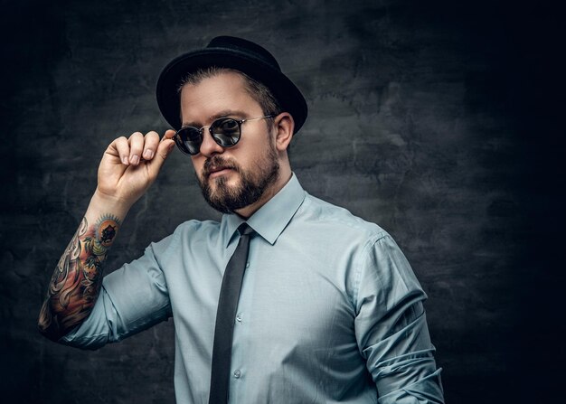 Portrait of bearded hipster dressed in a white shirt with bow tie and a hat.