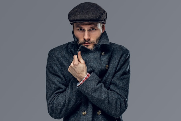 Free photo portrait of a bearded hipster man dressed in a gray jacket and a wool cap isolated on grey background.