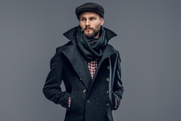 Portrait of bearded male dressed in a grey jacket and a hat isolated on grey background.