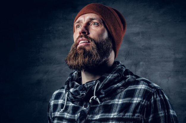 Portrait of bearded male in a hat and fleece shirt over dark grey background.