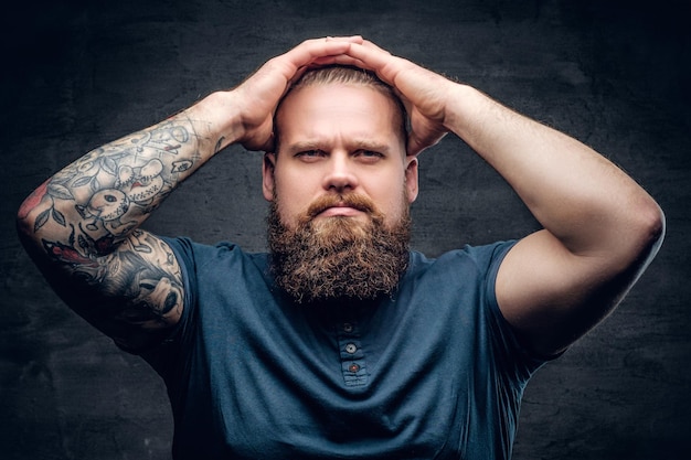 Portrait of bearded male touches his hairstyle with tattooed arms.