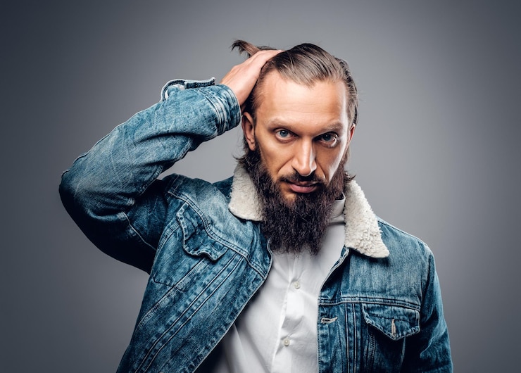 Free Photo portrait of bearded male with long hair dressed in a denim jacket, isolated on grey background.