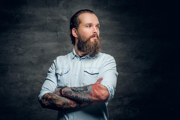 Free photo portrait of bearded male with tattooed crossed arms on grey background.