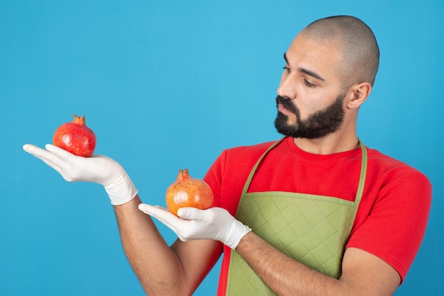Portrait of a bearded man in apron holding two fresh pomegranates in hands . 