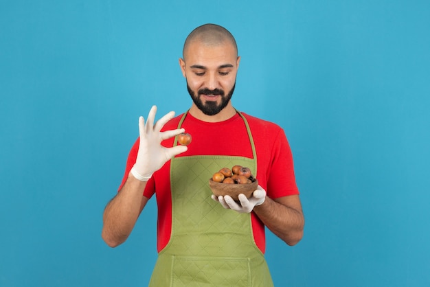 Portrait of a bearded man in apron holding a wooden bowl of dried fruits . 