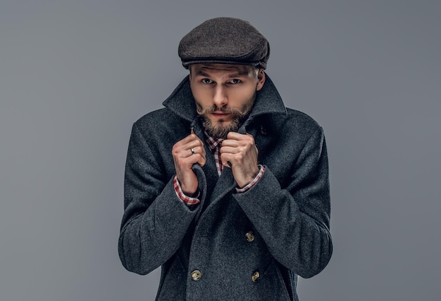 Portrait of a bearded man dressed in a worm jacket and wool cap isolated on grey background.