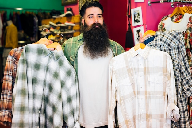 Portrait of bearded man holding shirts in the coat hanger