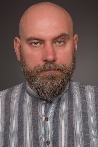 Free photo portrait of bearded man in prison garb. bold serious man in lined shirt posing on dark grey.