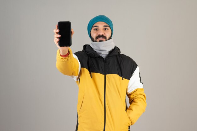 Портрет бородатого мужчины в теплой одежде, показывая свой мобильный телефон