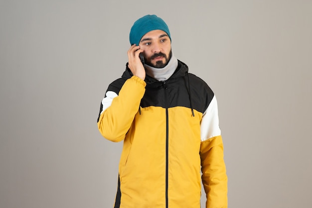Портрет бородатого мужчины в теплой одежде разговаривает по мобильному телефону.